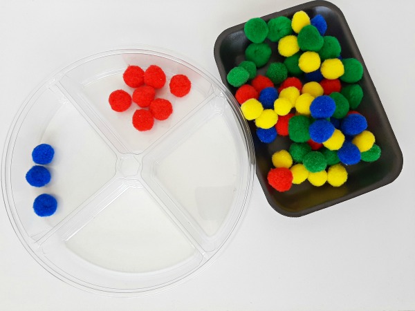 A divided tray and pompoms prompt a color sorting activity