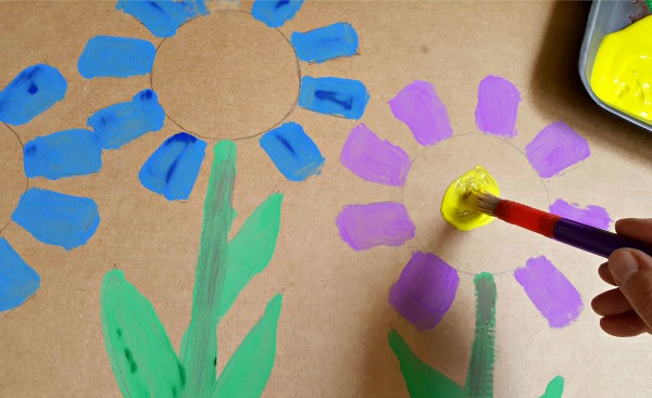 Paint flowers on a cardboard backdrop for a homemade marionette theater.
