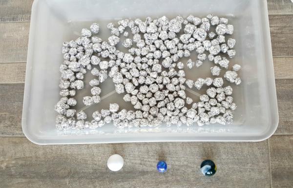 small pieces of aluminum foil rolled into balls are added to a small sensory bin for a preschool STEAM activit